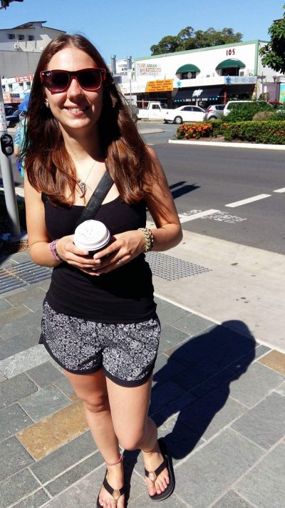 Chiara standing on the side of the street smiling and holding a coffee cup. 