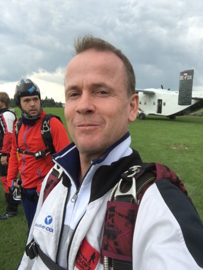 Dr Gobel takes a selfie while wearing a jumpsuit and skydiving rig.