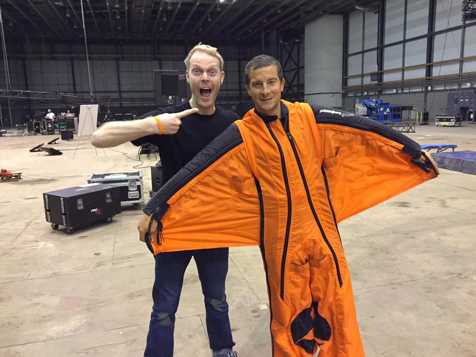 James poses with Bear Grylls who is wearing an orange wingsuit.