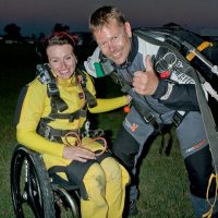 Marcus poses with a tandem student after a jump and gives a thumbs up.