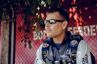 Marcus sitting on a bench in his skydiving gear waiting to board an airplane.