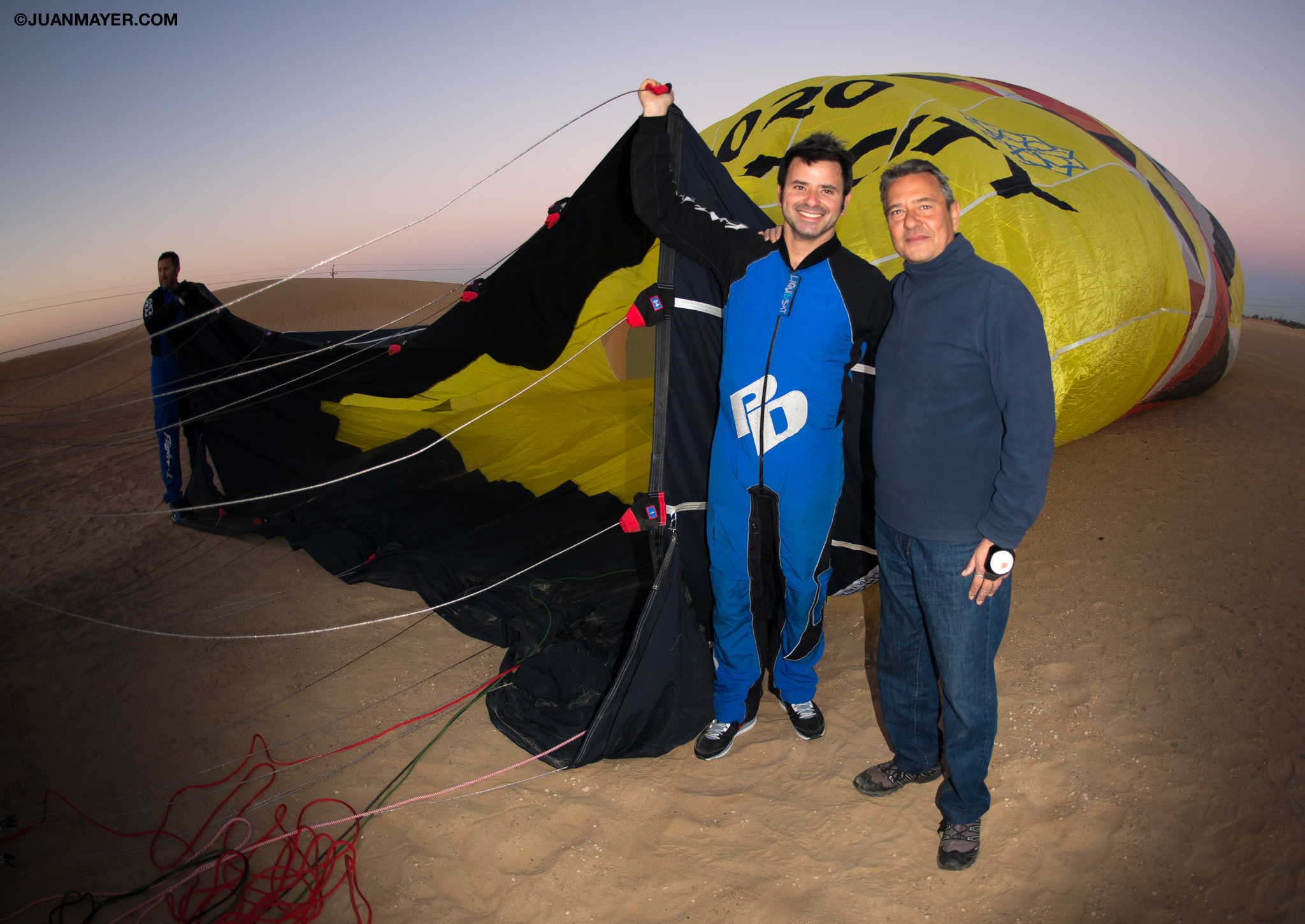 Juan takes his picture in front of a hot air balloon. 