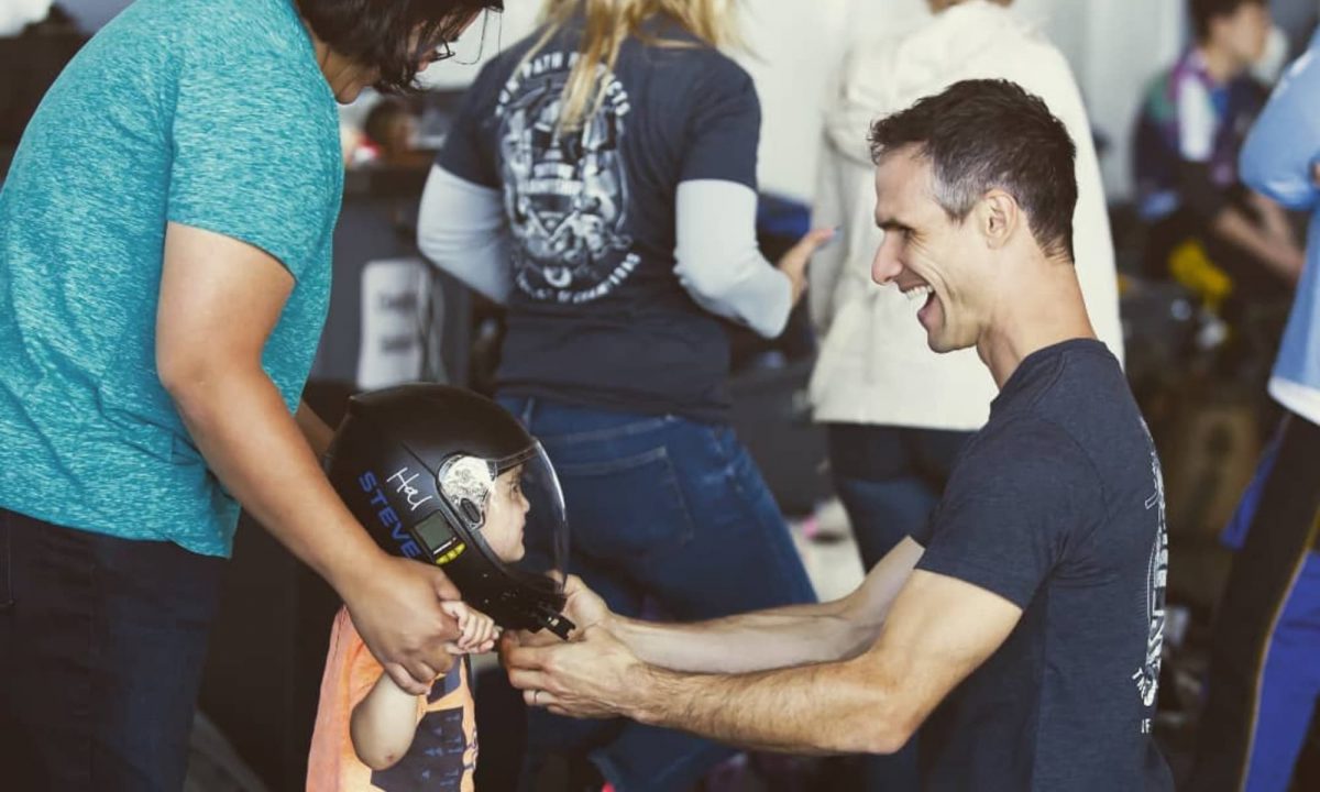 Steve smiles while putting his skydiving helmet on a little boy. 