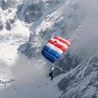 Omar flying under a red and blue parachute above a snow filled landscape with Mt. Everest in the background