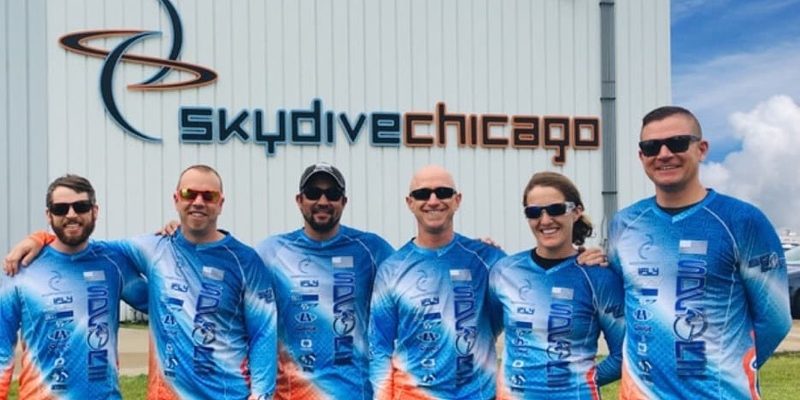 The six members of SDC Core smile together in their SDC Core team jerseys in front of the hangar at Skydive Chicago.