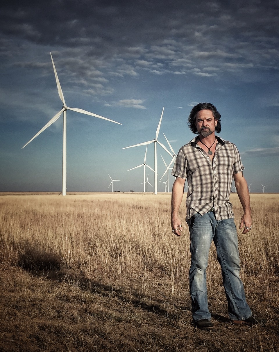 JayMo poses in front of a field of wind turbines