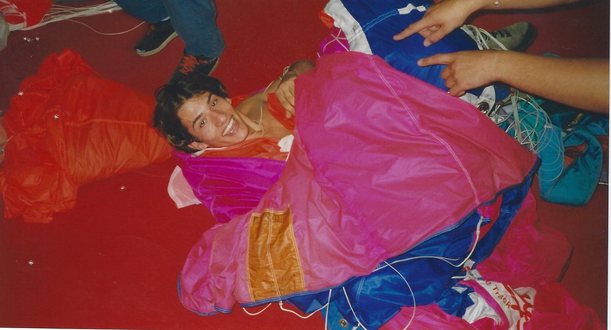 A young Fred Fugen smiles while laying on a parachute on the packing mat