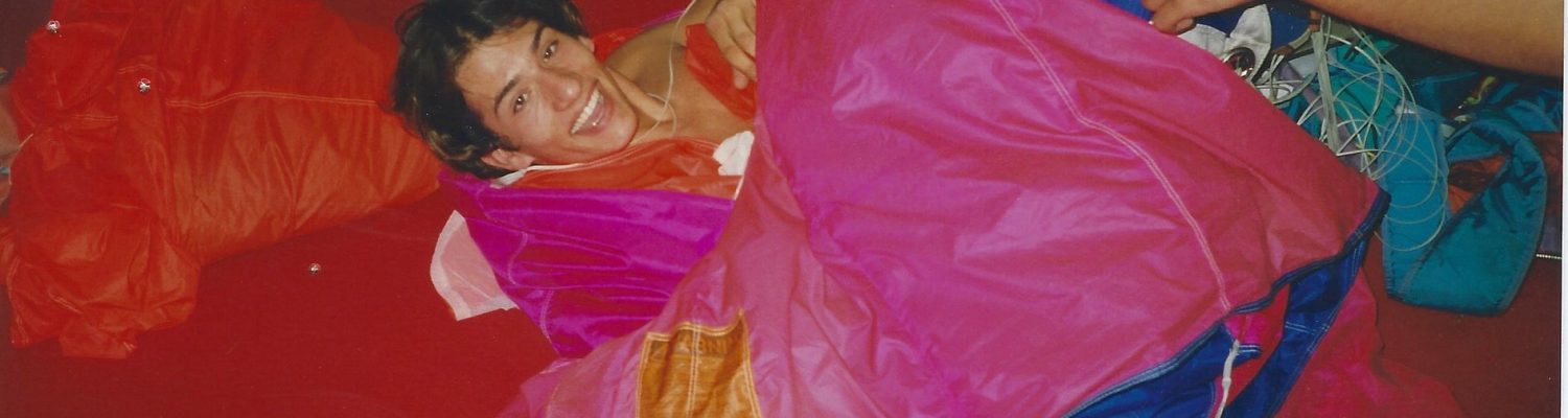 A young Fred Fugen smiles while laying on a parachute on the packing mat