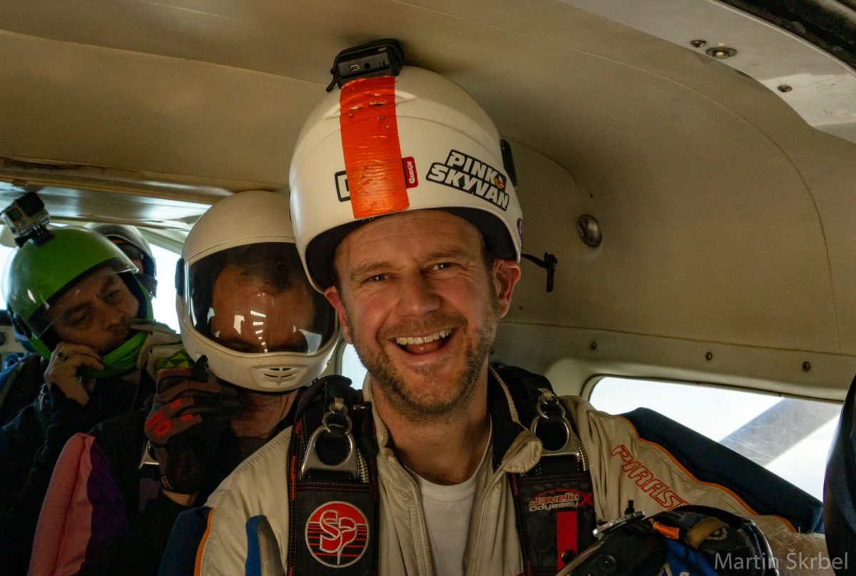 Brian Cumming smiles while sitting in a jump plane flying to altitude
