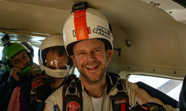 Brian Cumming smiles while sitting in a jump plane flying to altitude